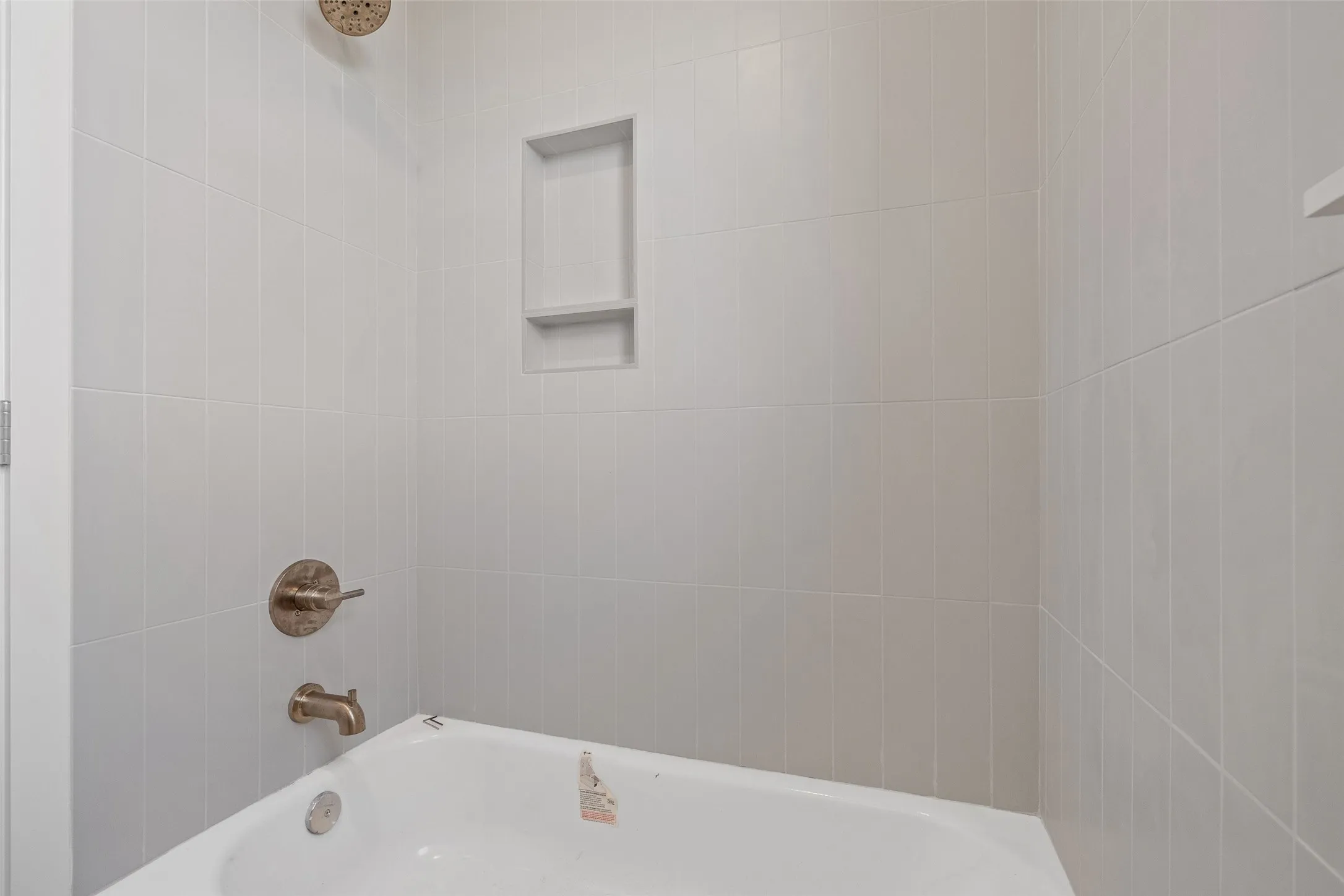 Bathtub with white subway tile surround, integrated shower niche, and brushed brass fixtures