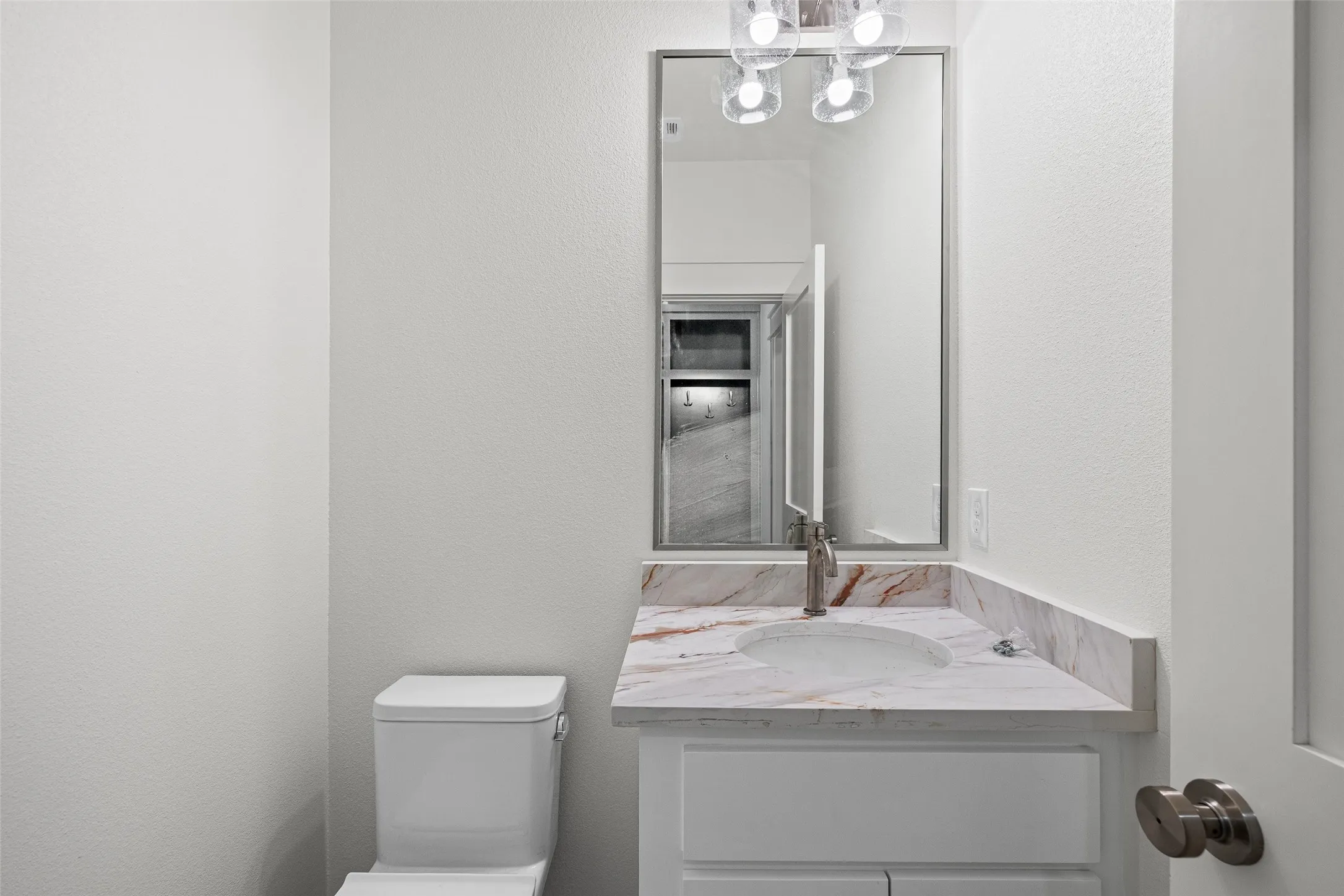 Bathroom vanity featuring a vessel sink set into a patterned countertop, a wall-mounted mirror, and a contemporary light fixture