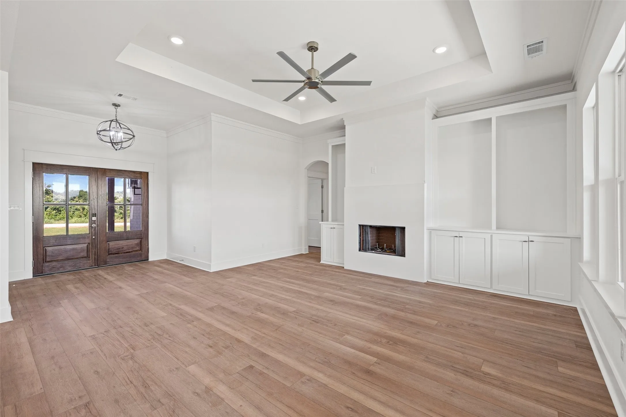 Spacious living area featuring wood-finish flooring, a tray ceiling with recessed lighting, and a modern ceiling fan