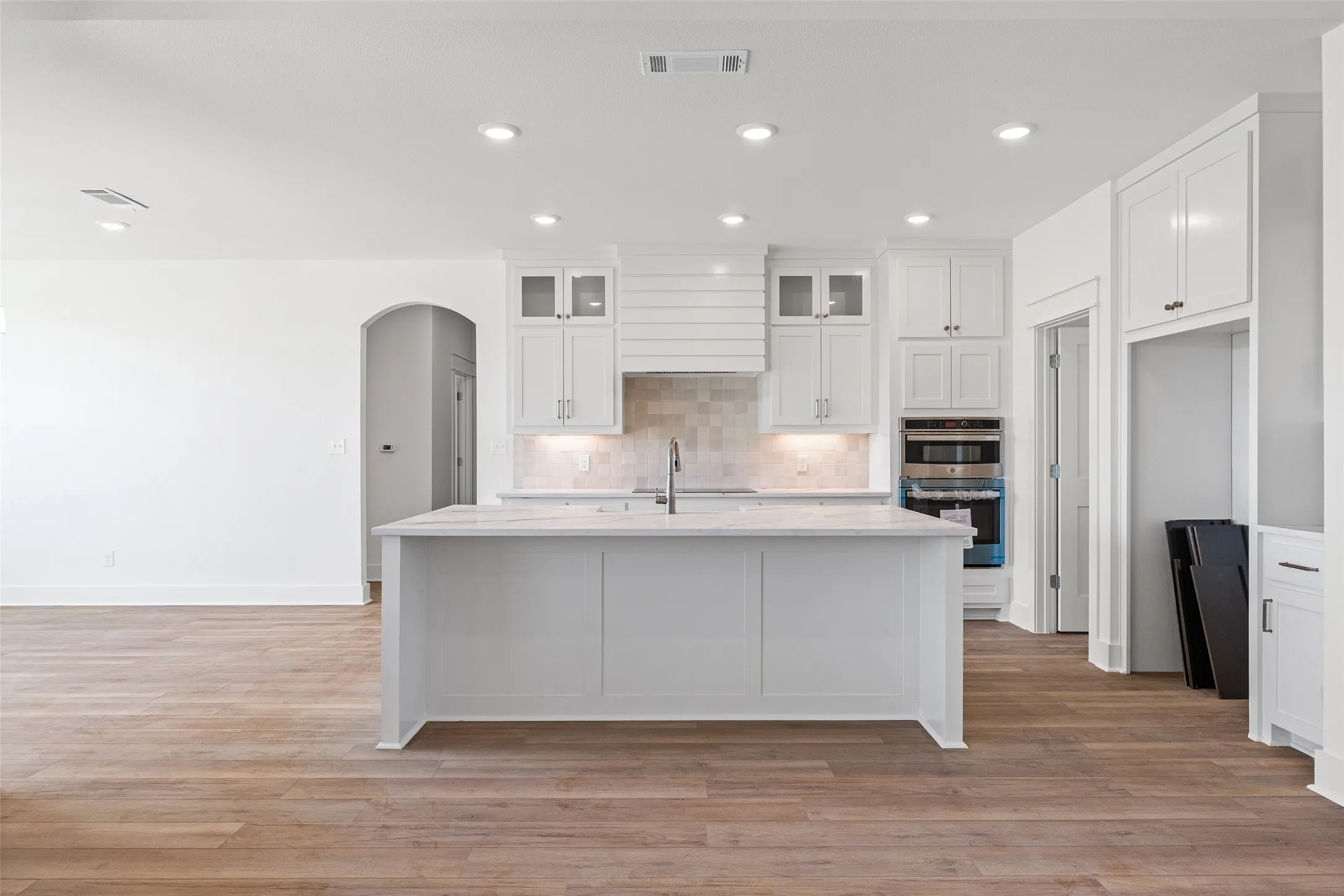 Modern kitchen featuring a central island, white cabinetry, integrated stainless steel appliances, a tile backsplash, and recessed lighting