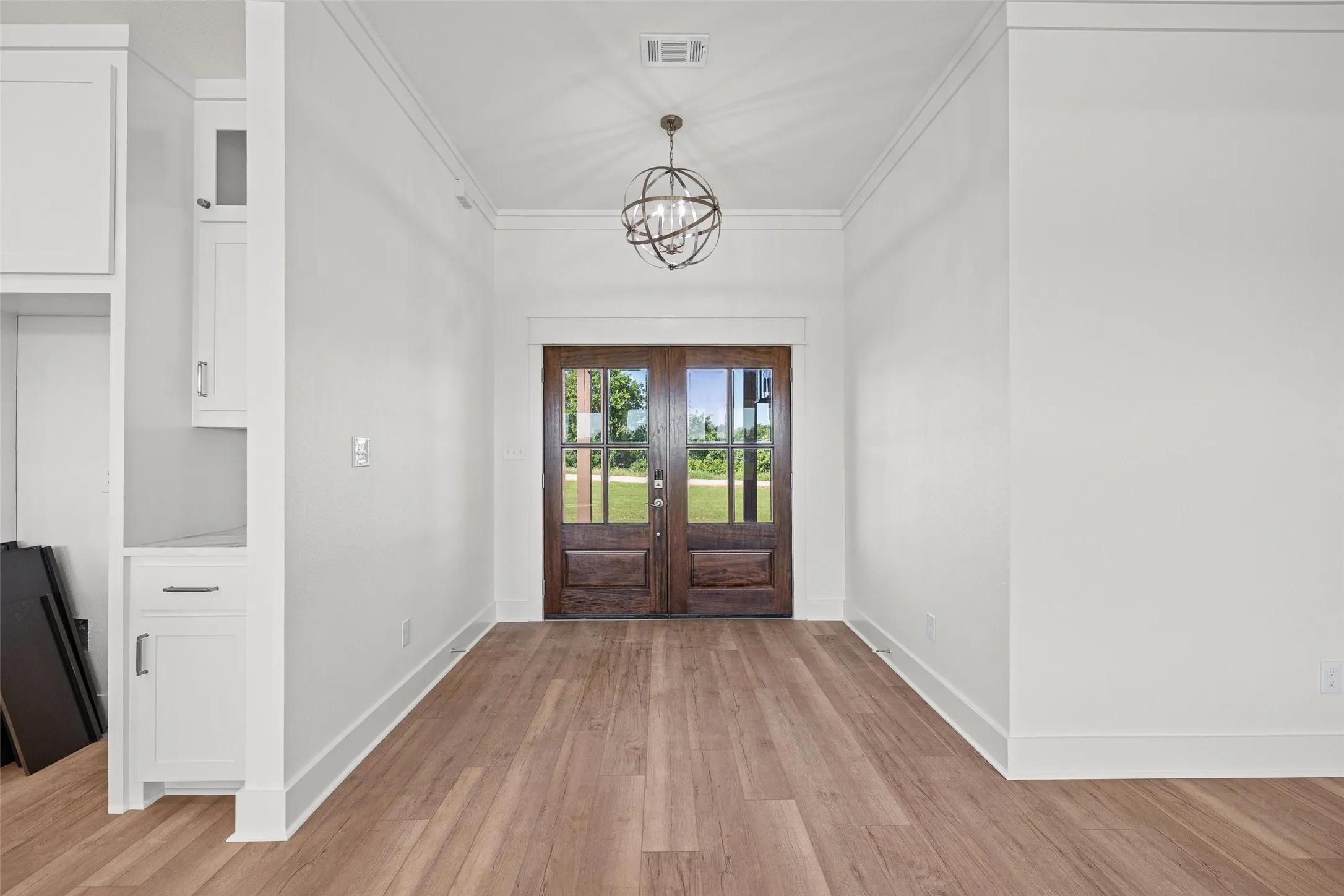 Double entry doors with divided lites, wood-finish flooring, recessed lighting, crown molding, and built-in cabinetry