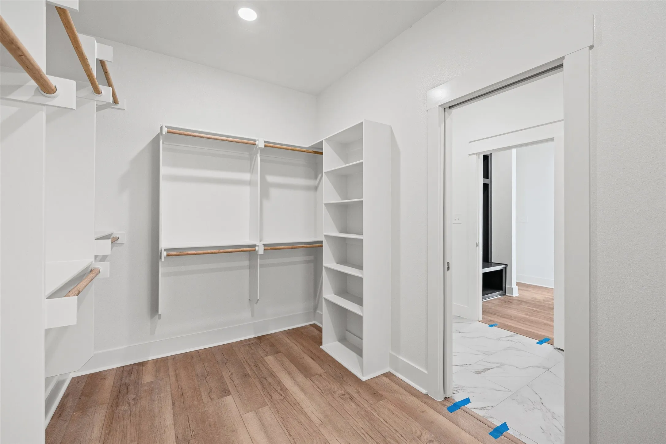 Spacious walk-in closet featuring wood-finish flooring, white walls, recessed ceiling lighting, built-in shelving, and multiple hanging rods