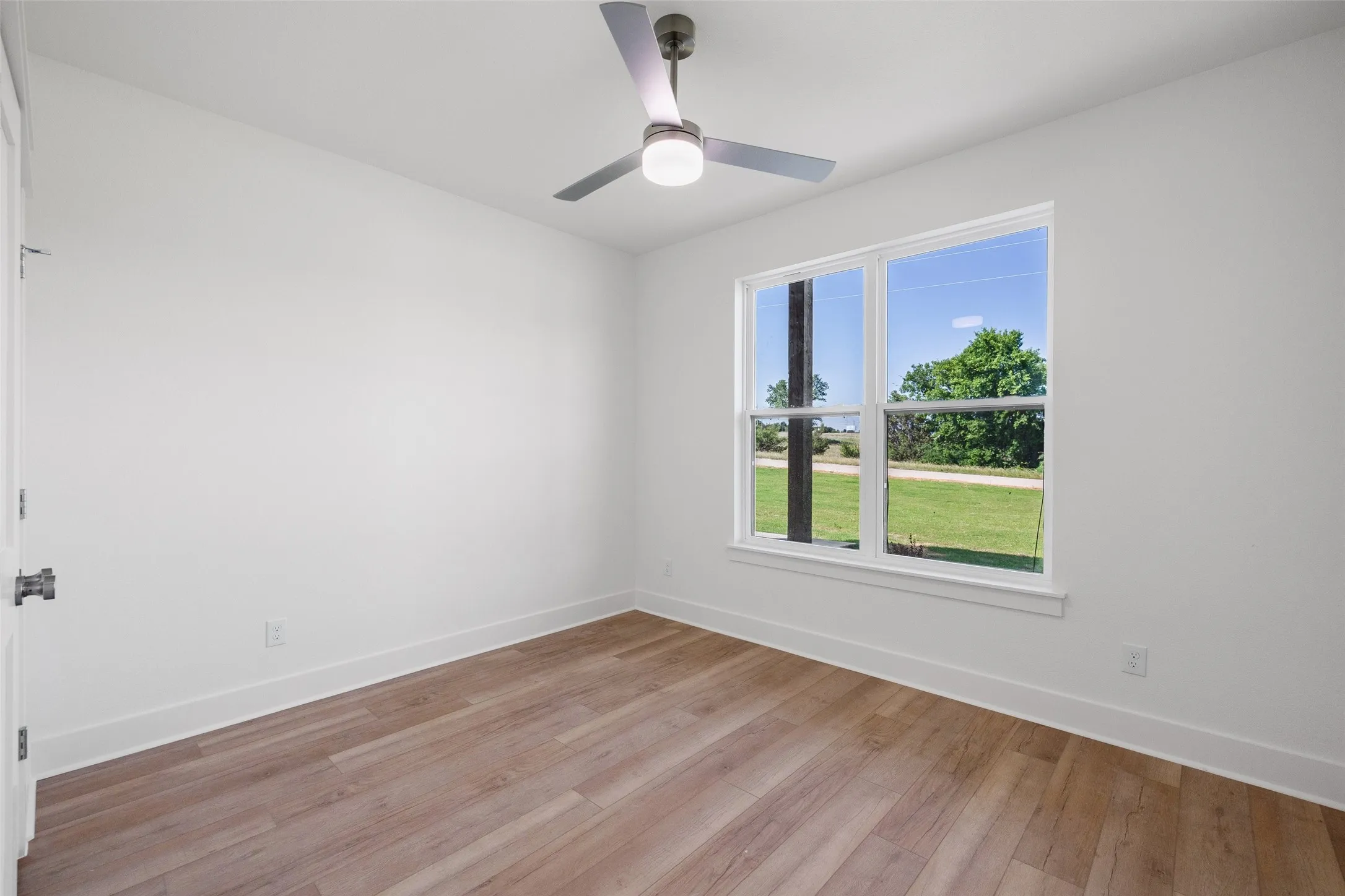 Bright room with wood-finish flooring, white walls, and a modern ceiling fan with integrated lighting