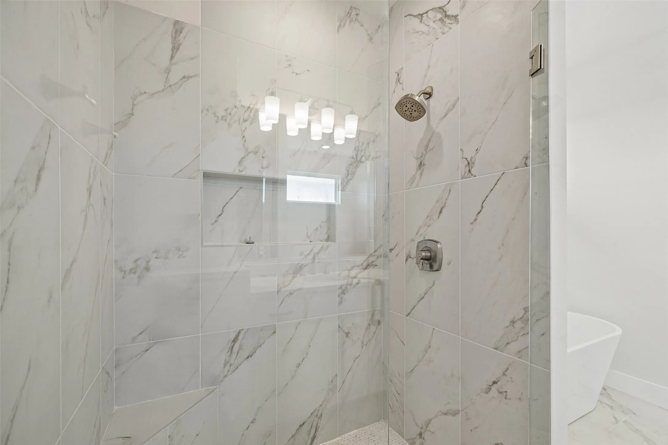 Walk-in shower featuring large format marbled tile, a built-in shower niche, and a rain showerhead