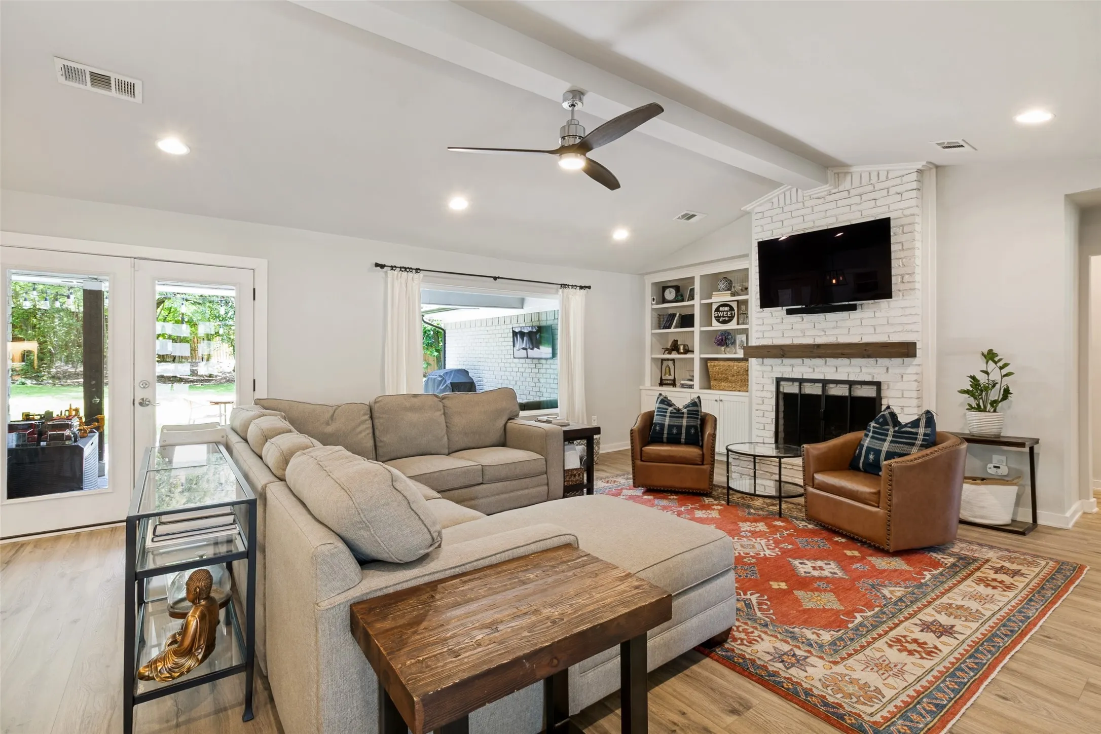 Expansive living room with vaulted ceilings, abundant natural light, and a striking floor-to-ceiling brick fireplace as the focal point.