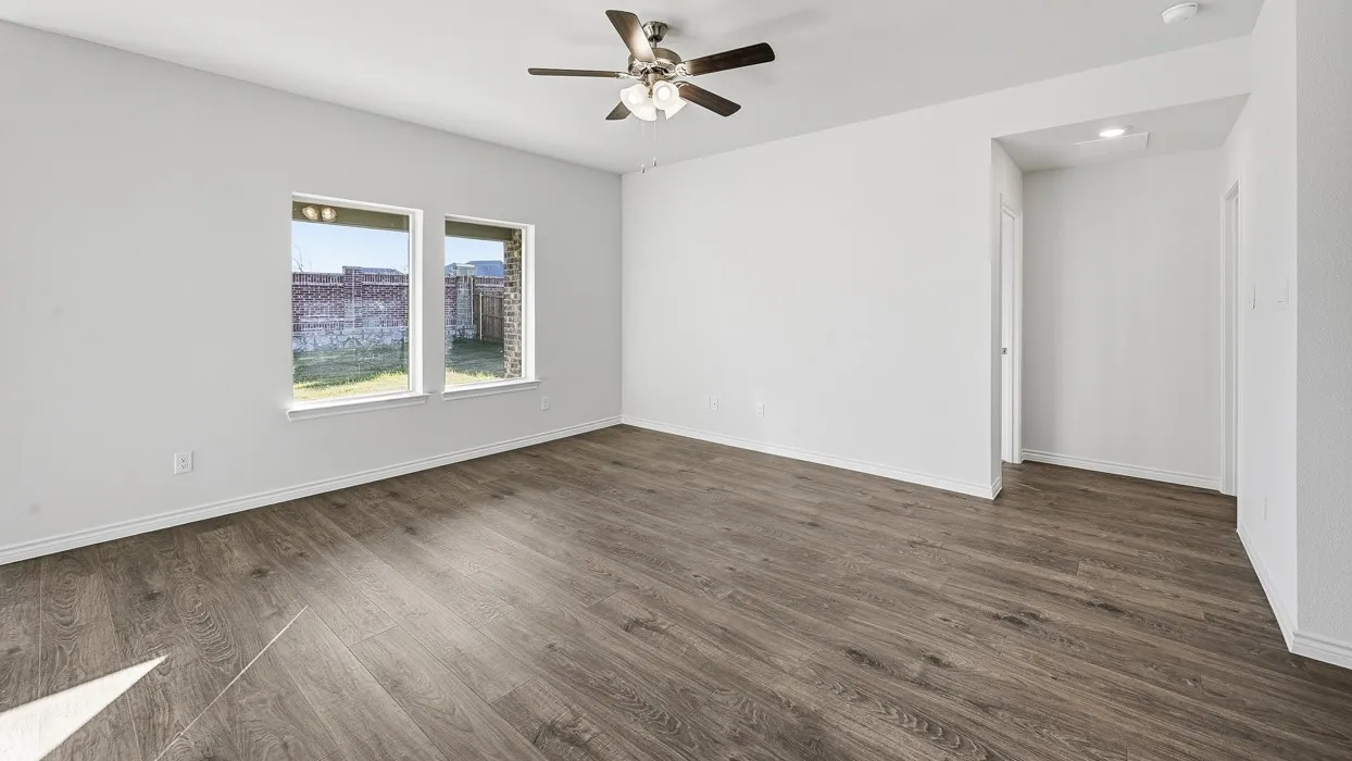 Spacious room featuring wood-finish flooring, two large windows, a ceiling fan with integrated lighting, and a white interior door