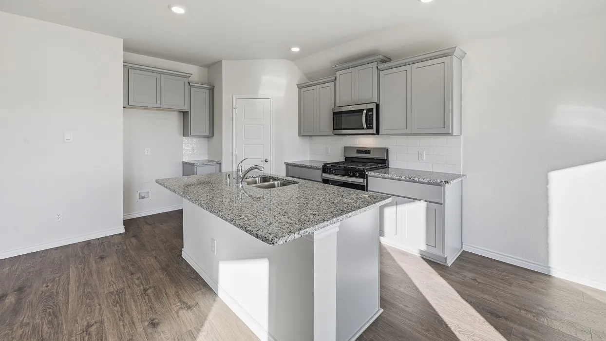 Kitchen featuring a central island with a double basin sink and granite-style countertop, complemented by light gray cabinetry, stainless steel appliances, and a white subway tile backsplash