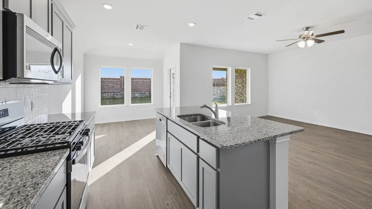 Open-concept kitchen and living area featuring granite countertops, a kitchen island with a double sink, stainless steel appliances, and wood-finish flooring
