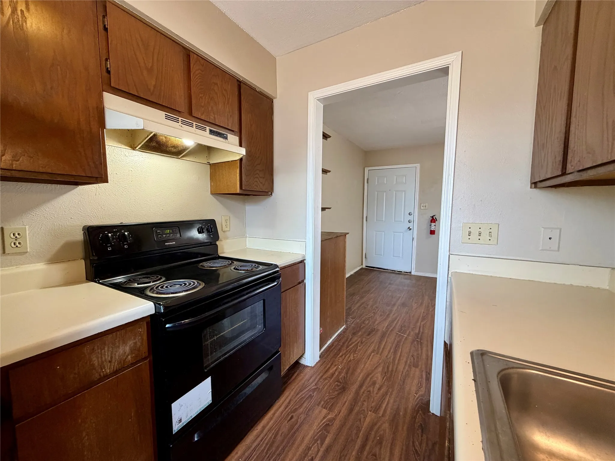 Kitchen featuring wood-finish flooring, dark wood cabinetry, white countertops, and a black electric range with an overhead exhaust fan