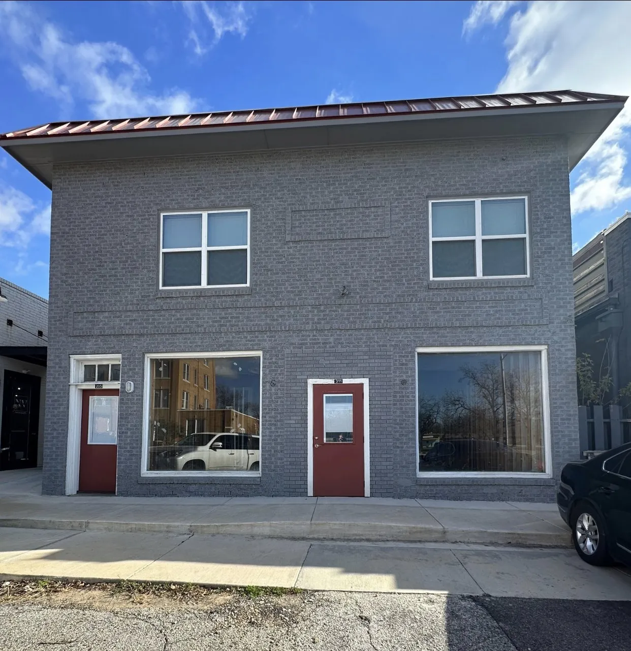 Two-story commercial building featuring a gray brick exterior, red entry doors, and a brown metal roof