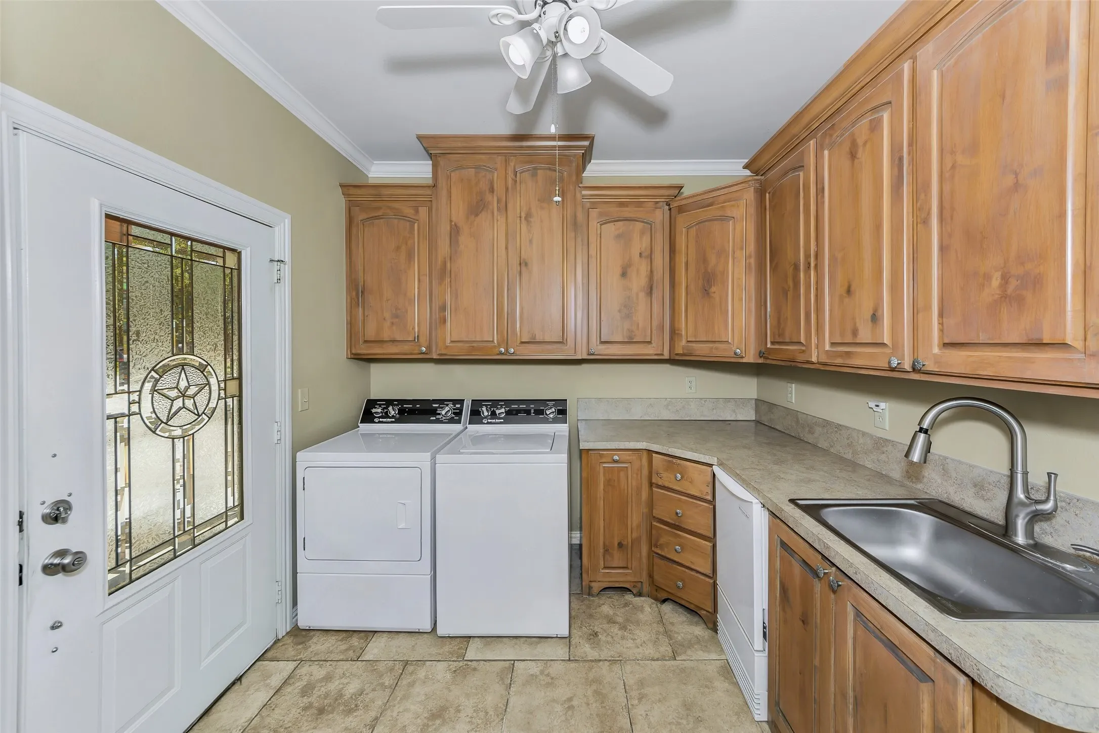 Functional utility room featuring wood-finish cabinetry, a utility sink with a gooseneck faucet, and tile flooring