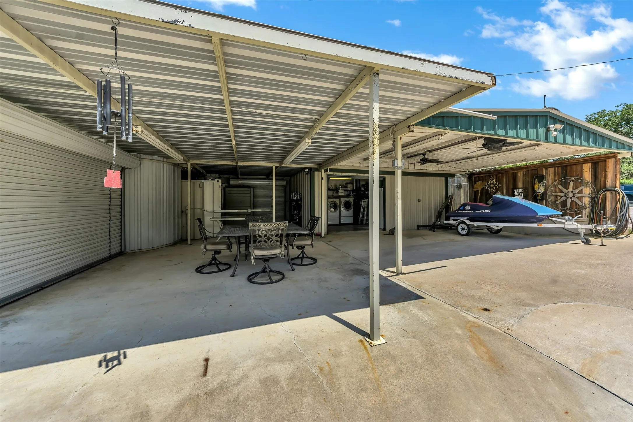 Expansive covered concrete patio featuring a dining area, an outdoor laundry station, and additional covered parking