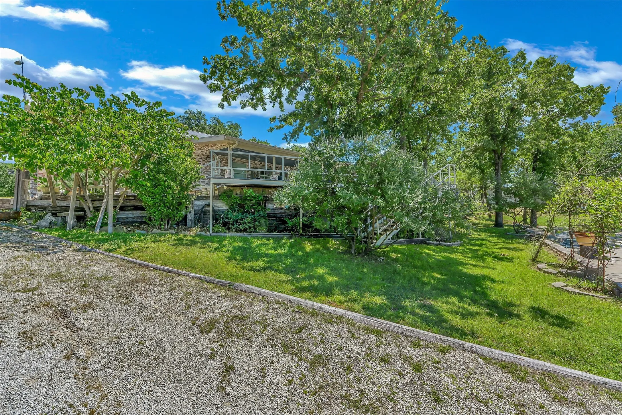 Elevated exterior featuring a screened-in porch, extensive decking, natural wood siding, and mature trees