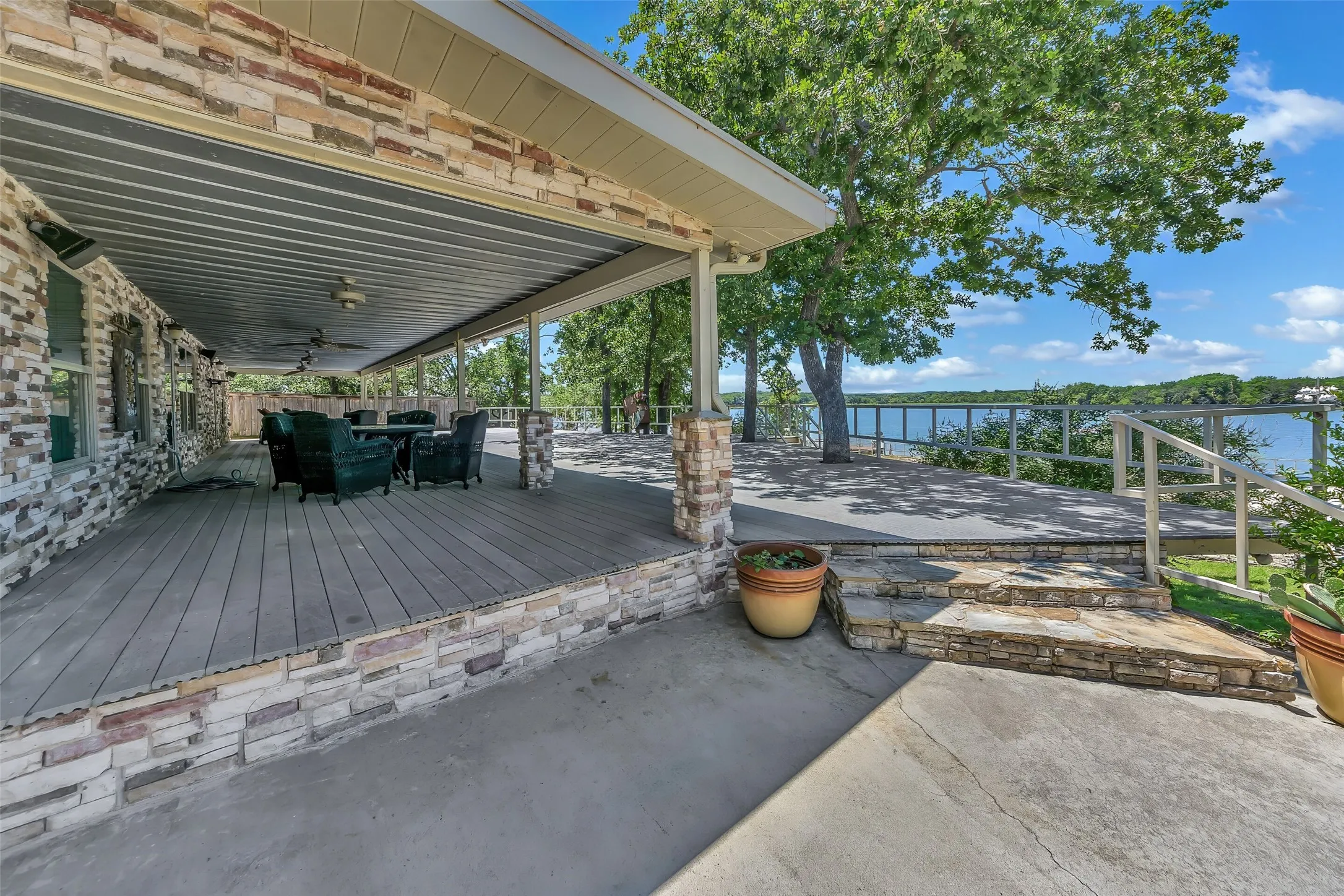 Expansive covered patio featuring a planked deck surface, stone veneer accents, and ceiling fans