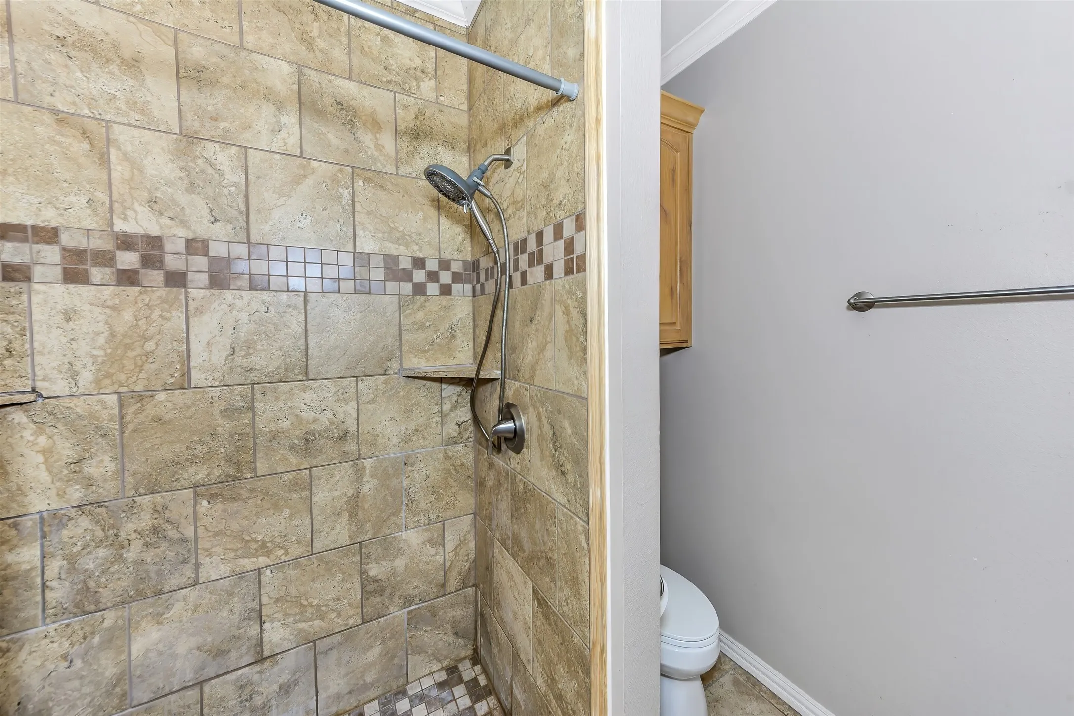 Shower with floor-to-ceiling ceramic tile, decorative mosaic tile accent band, built-in shower shelf, and brushed nickel fixtures