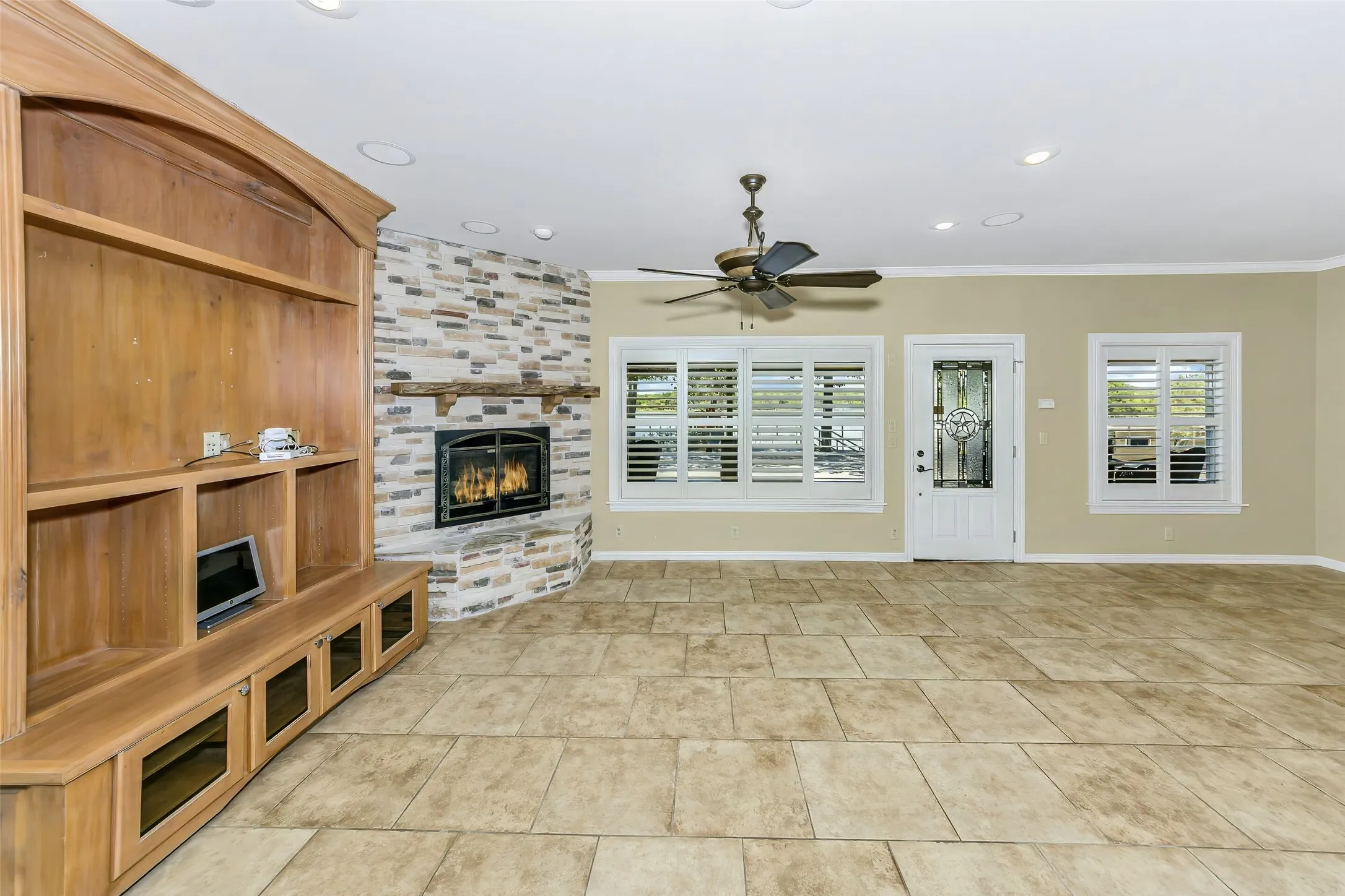 Spacious living area featuring a corner fireplace with stone surround, a built-in entertainment center, tile flooring, recessed lighting, and a ceiling fan