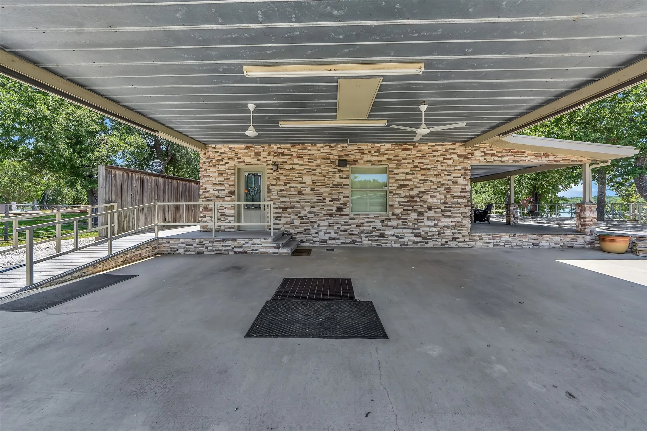 Covered concrete parking area featuring a stone veneer exterior wall, a glass-paned entry door, and a window with blinds