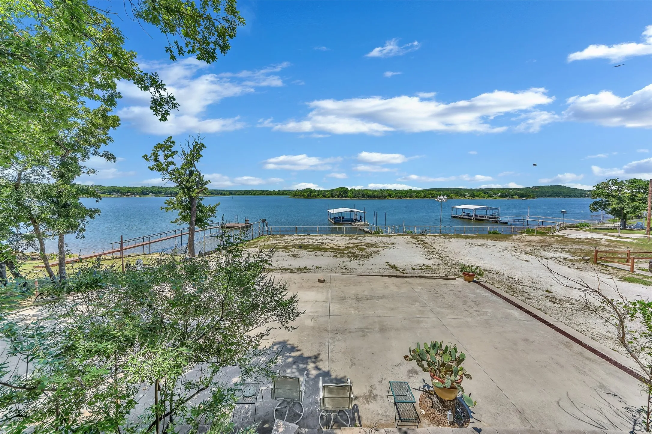 Expansive lakefront property featuring extensive concrete paving, a fenced perimeter, and established landscaping