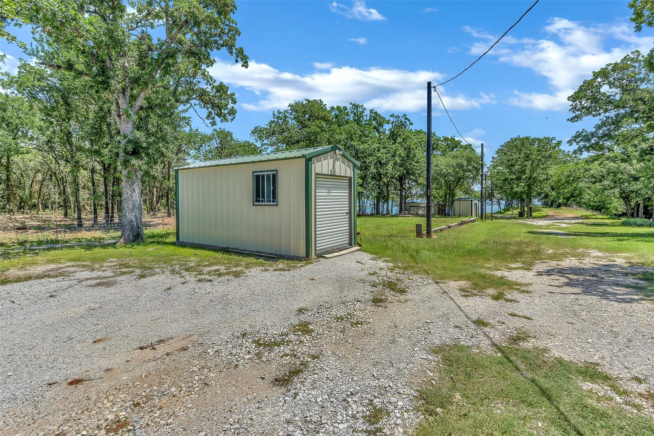 Metal outbuilding with a roll-up door, side window, and green trim, set on a gravel drive
