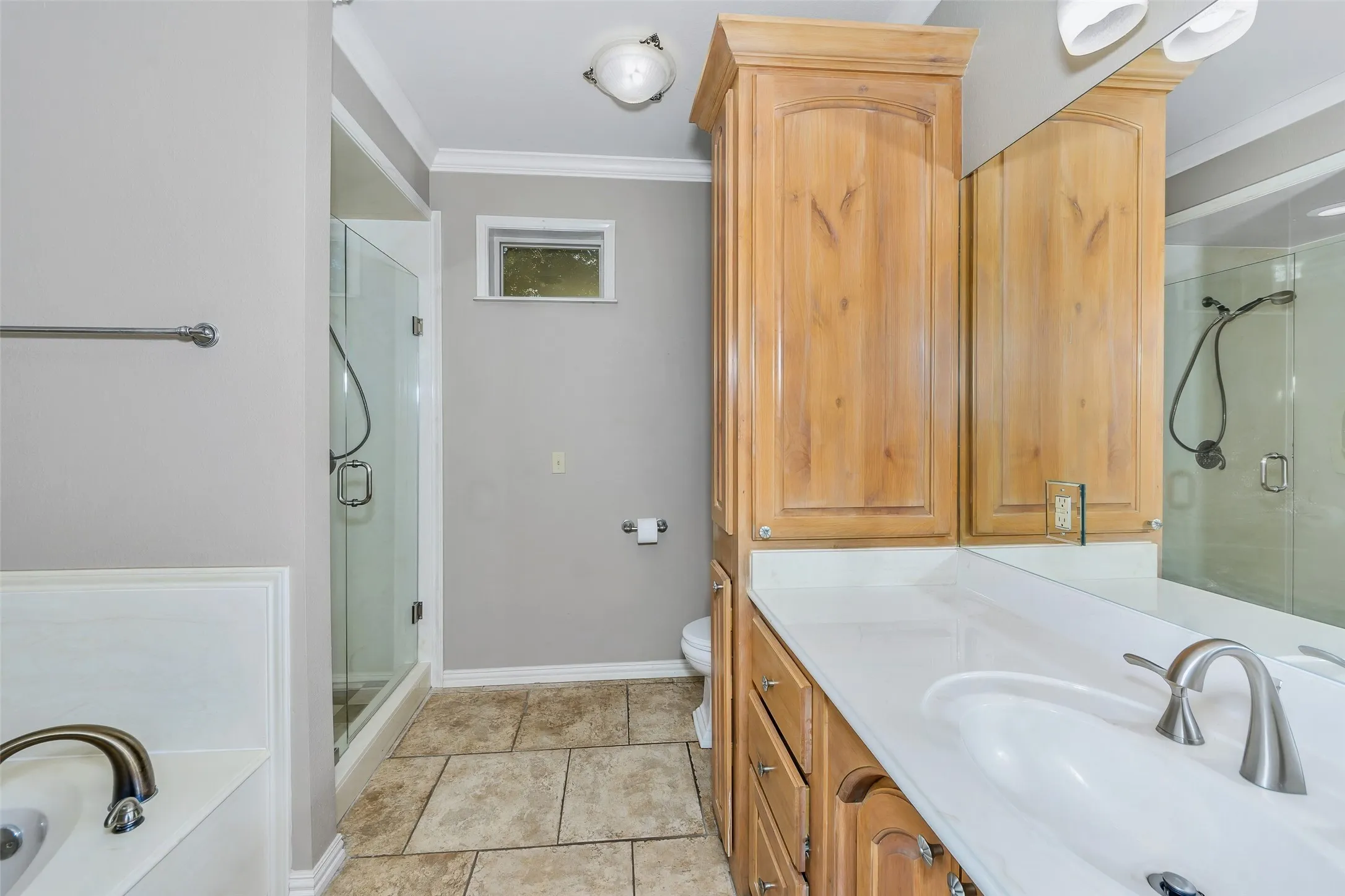 Bathroom featuring a glass-enclosed shower, built-in wooden cabinetry, a white countertop vanity with an integrated sink, and large format floor tiling