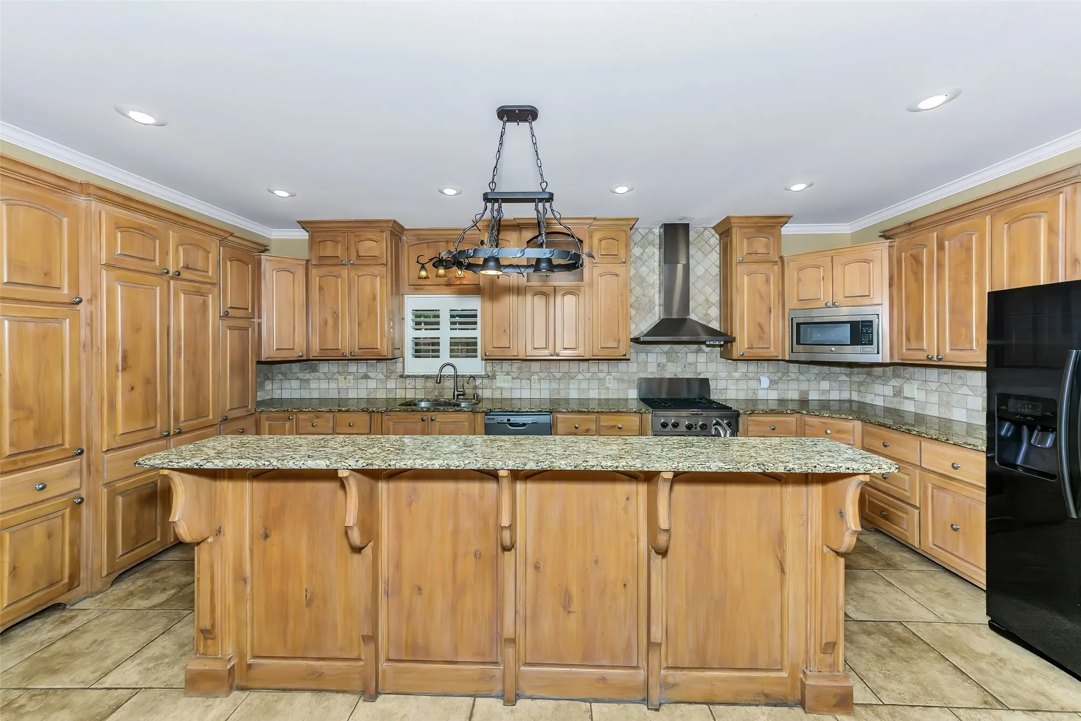Kitchen featuring a central island with a granite countertop, extensive light wood cabinetry, recessed lighting, and a stainless steel range hood