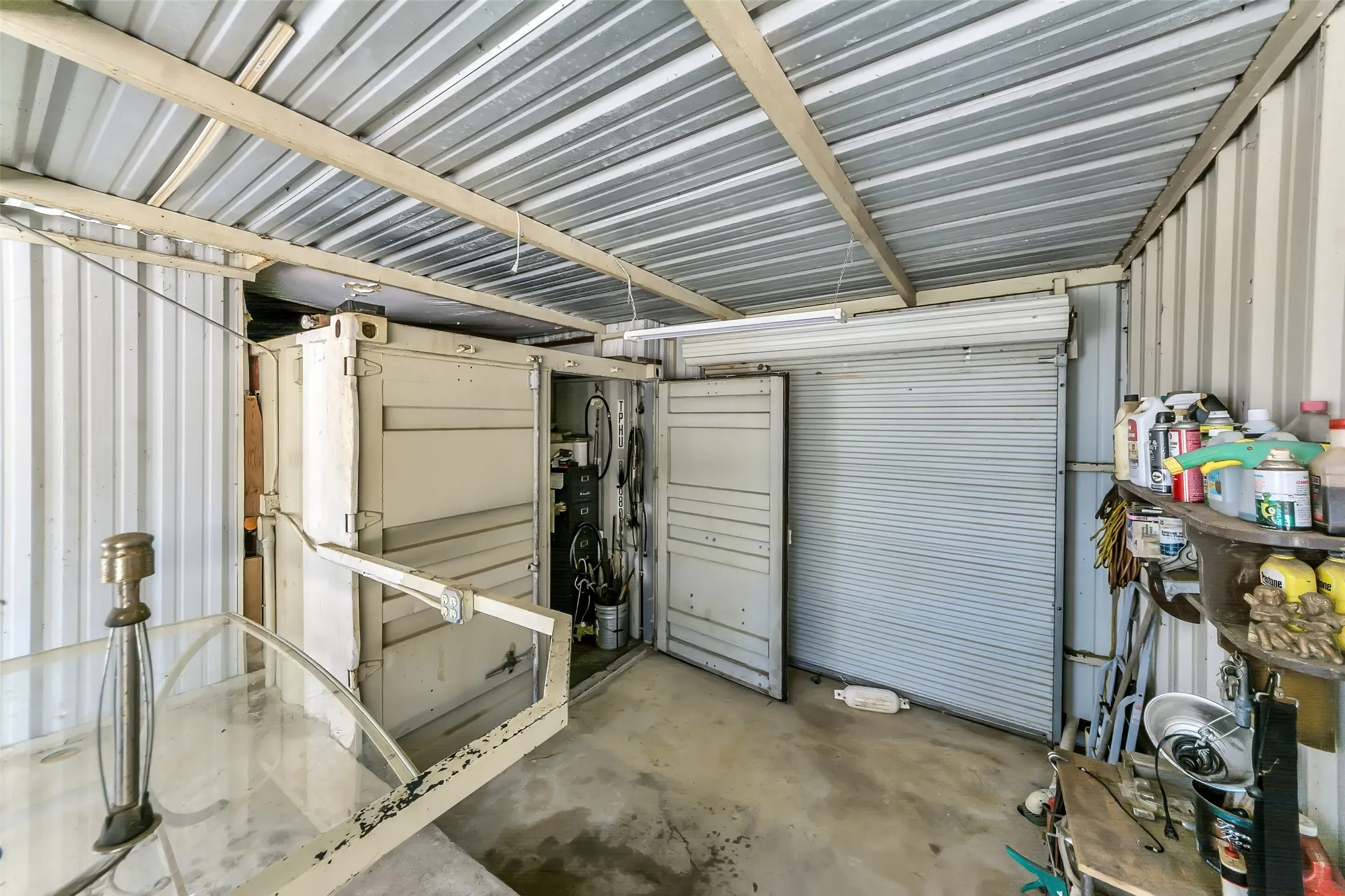 Covered outdoor area featuring a corrugated metal roof, exposed wooden support beams, and concrete flooring
