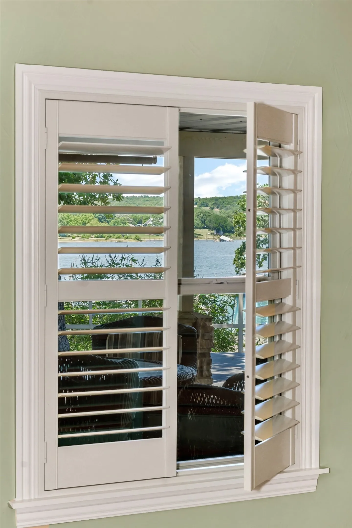 Window with louvered shutters, white trim, and a serene water backdrop