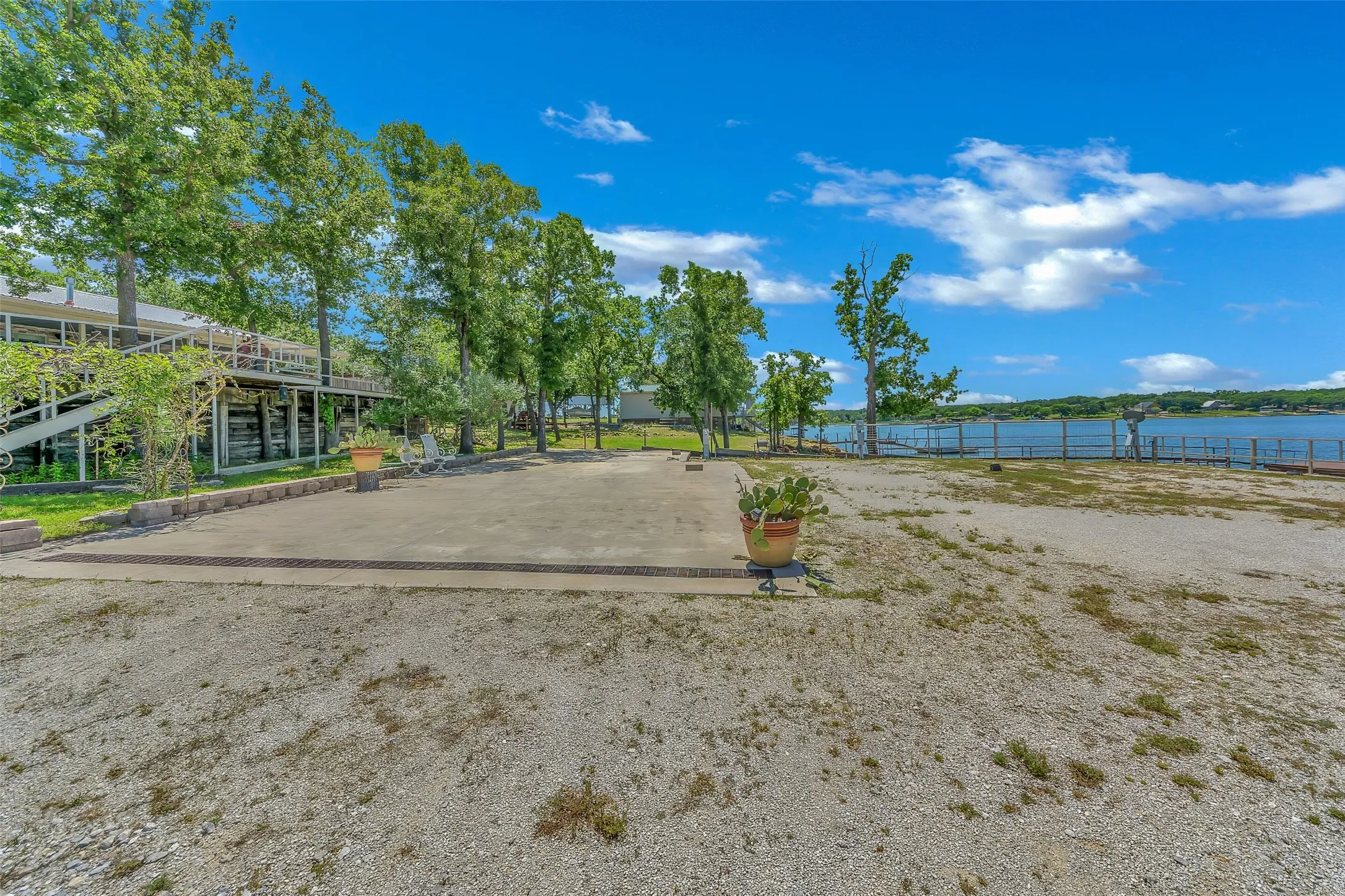 Waterfront property featuring a gravel lot, concrete pad, mature trees, and a multi-level deck structure