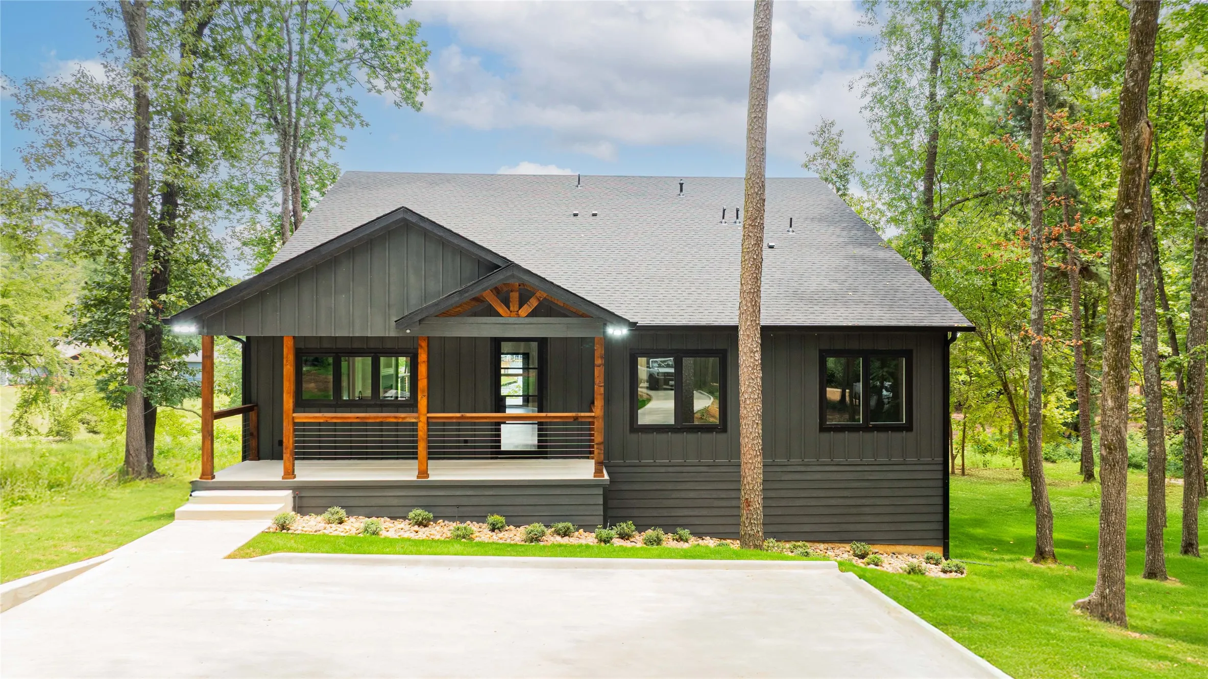 Modern farmhouse exterior featuring dark gray board-and-batten siding, a covered porch with natural wood posts, black-framed windows, and a concrete driveway