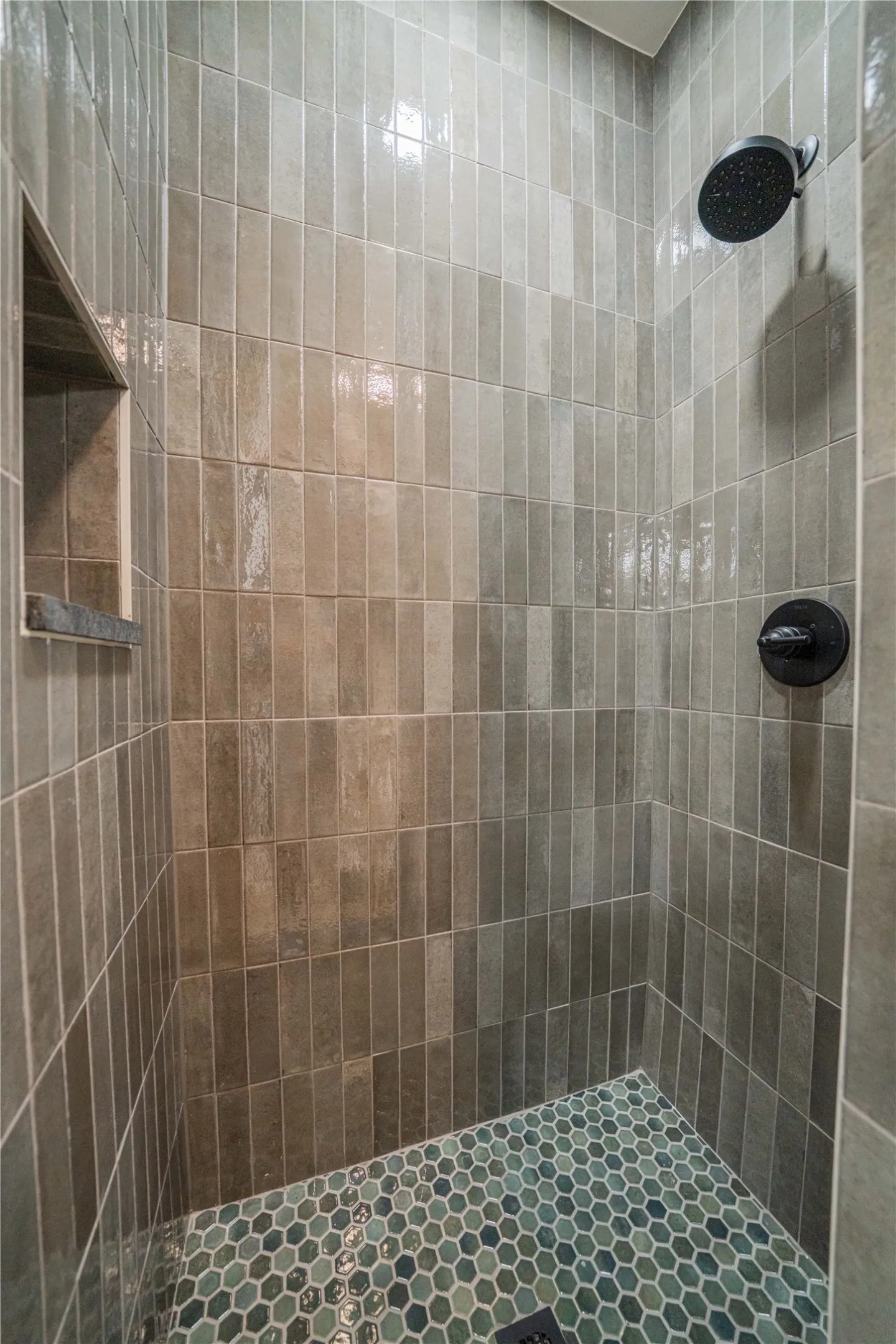 Shower enclosure featuring vertically stacked tile walls in varying shades of gray, a built-in shower niche with a stone sill, and a contrasting hexagonal mosaic tile floor