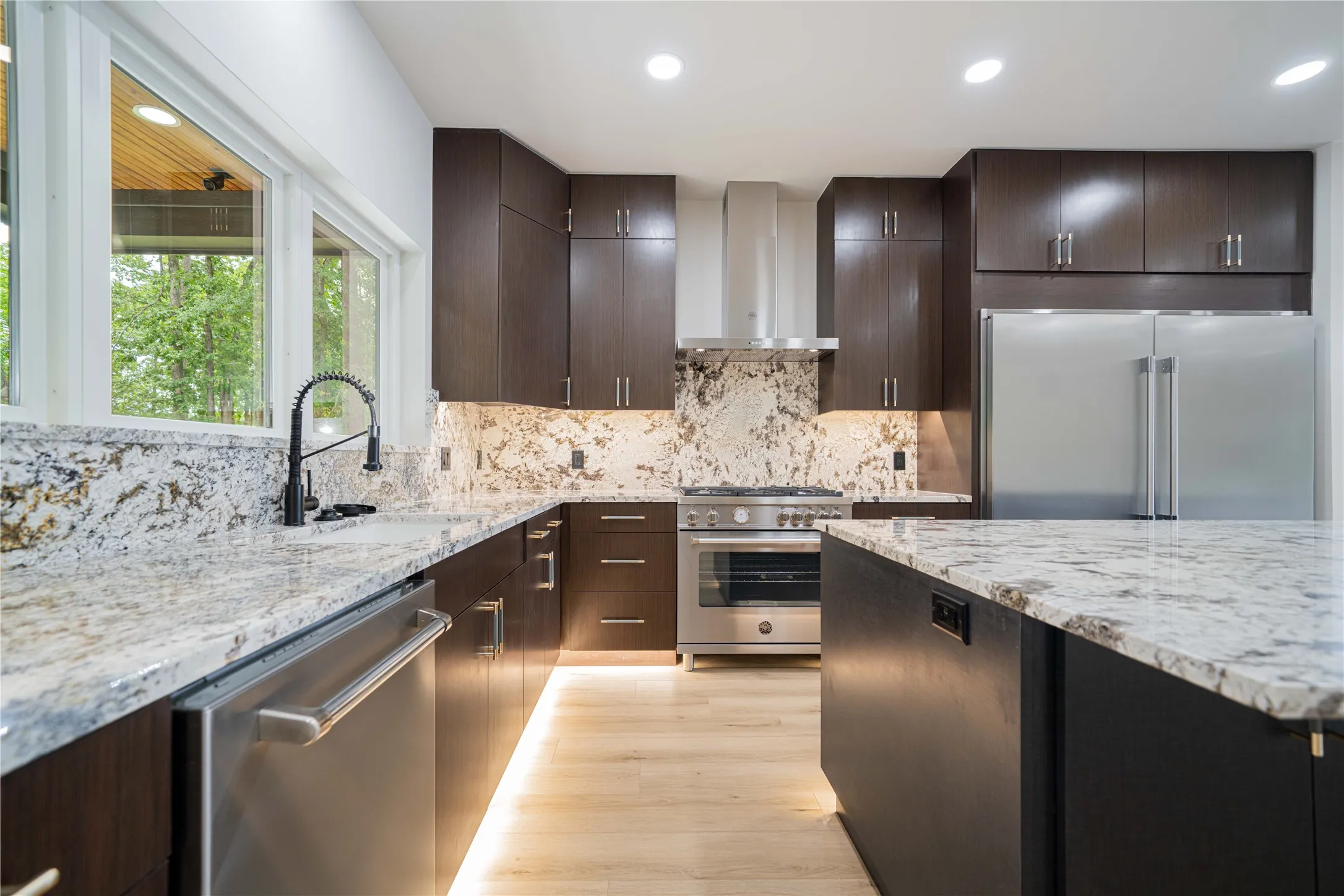Contemporary kitchen featuring dark wood cabinetry, light-toned stone countertops, and a matching stone backsplash