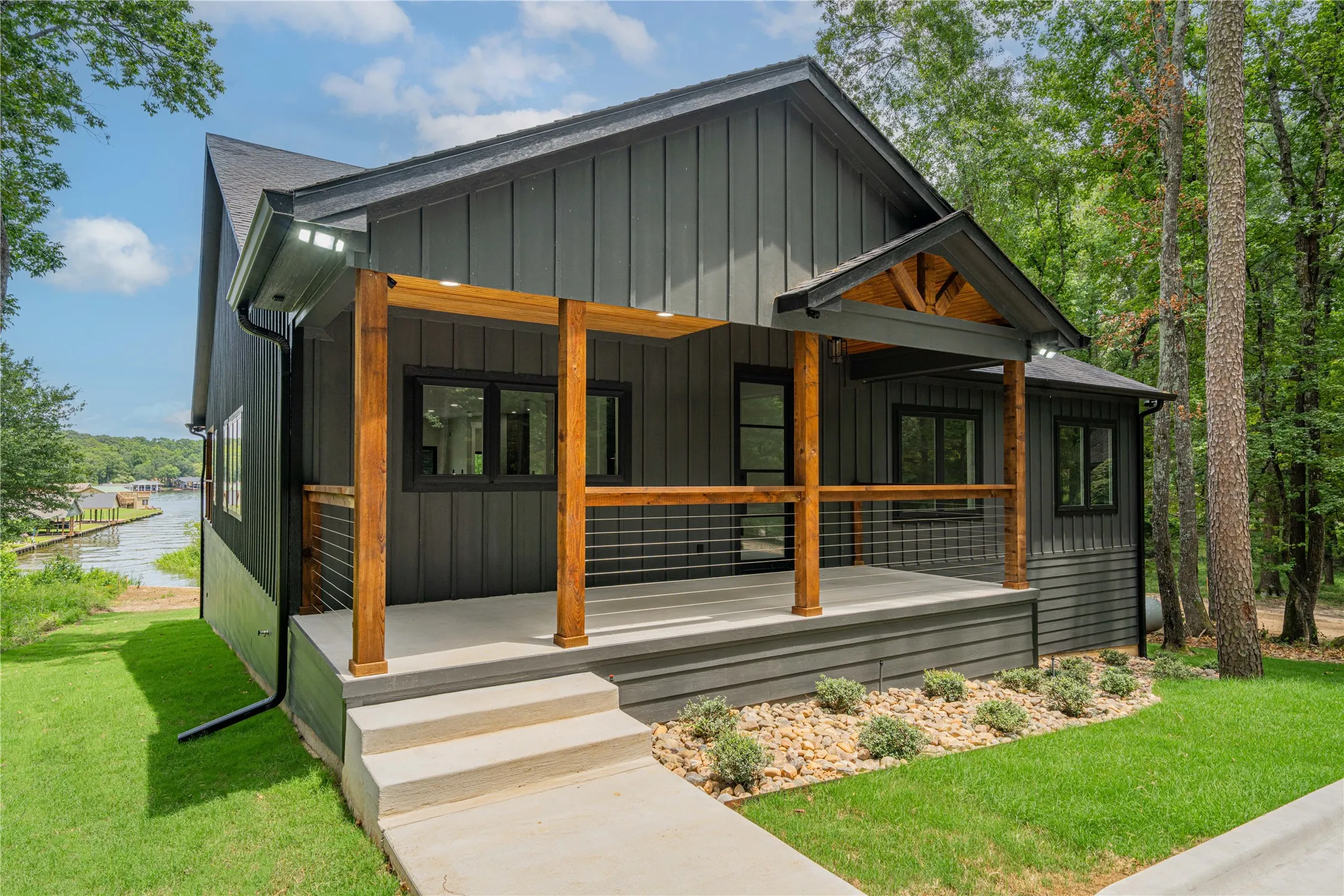 Modern exterior featuring dark gray board and batten siding with a covered concrete porch, natural wood posts, and cable railing