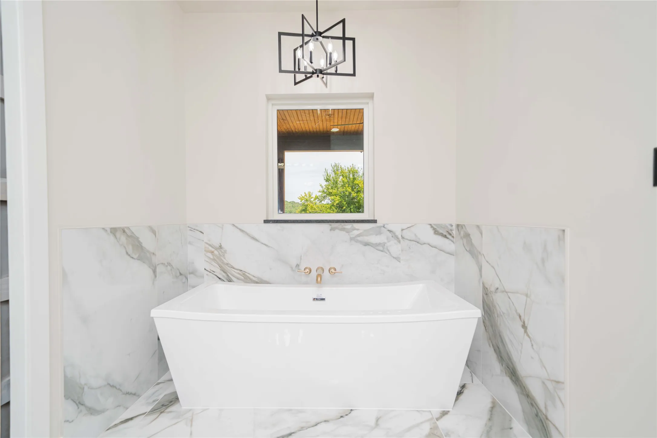 Freestanding soaking tub with gold-finish fixtures set against a white and gray veined tile surround