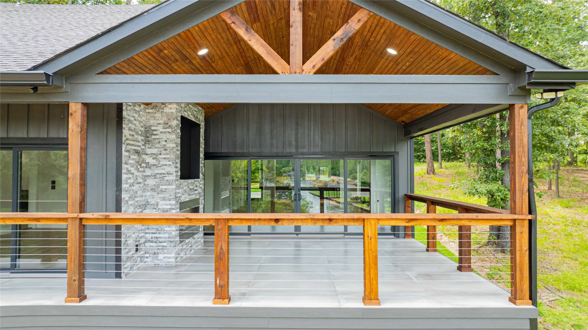 Covered outdoor living space featuring a wood-planked vaulted ceiling, recessed lighting, and a stone-clad fireplace