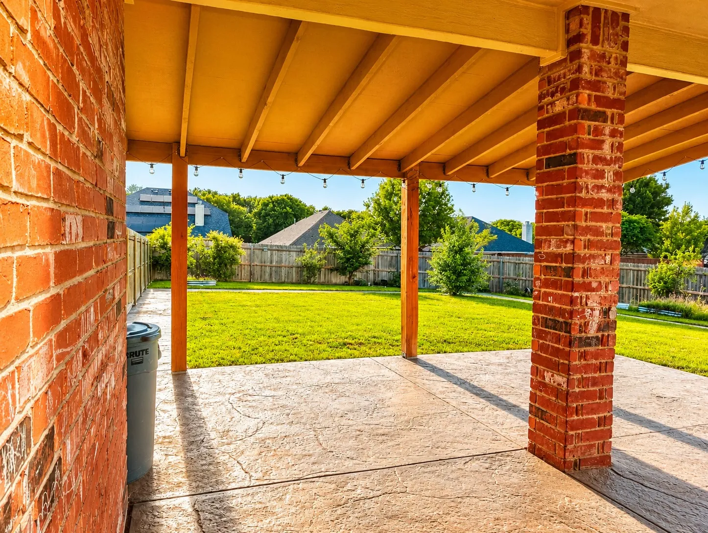 Covered patio featuring stamped concrete flooring, exposed wood beam ceiling, and brick columns