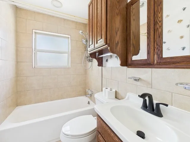 Full bath with tasteful backsplash, vanity, shower / tub combination, toilet, and tile walls