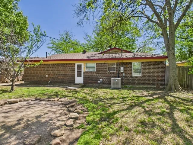 Back of property with central AC unit, fence, brick siding, and a yard