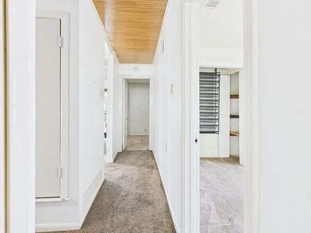 Hall with carpet, visible vents, baseboards, and wooden ceiling