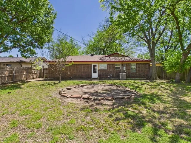 Rear view of property featuring brick siding, a fenced backyard, central air condition unit, and a lawn