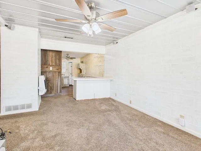 Unfurnished living room with a ceiling fan, carpet, and visible vents