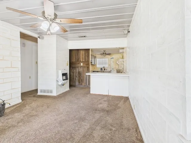 Unfurnished living room featuring carpet floors, ceiling fan, visible vents, and heating unit