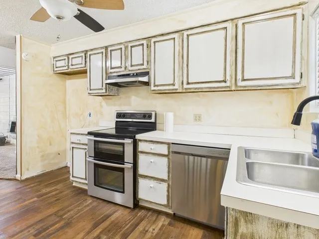 Kitchen featuring light countertops, under cabinet range hood, dark wood-type flooring, stainless steel appliances, and a sink