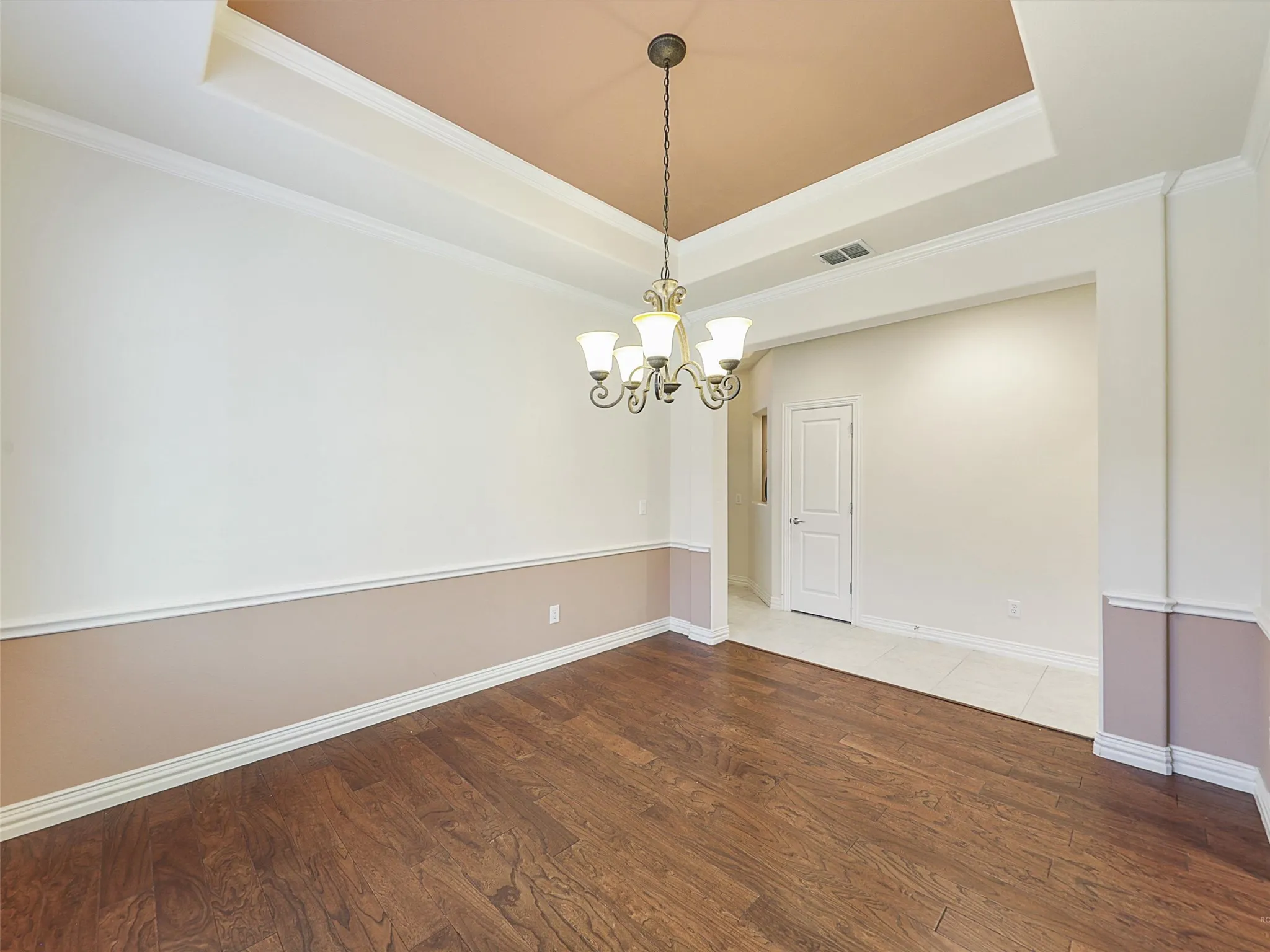 Dining room featuring a tray ceiling, wood finished floors, ornamental molding, and a chandelier