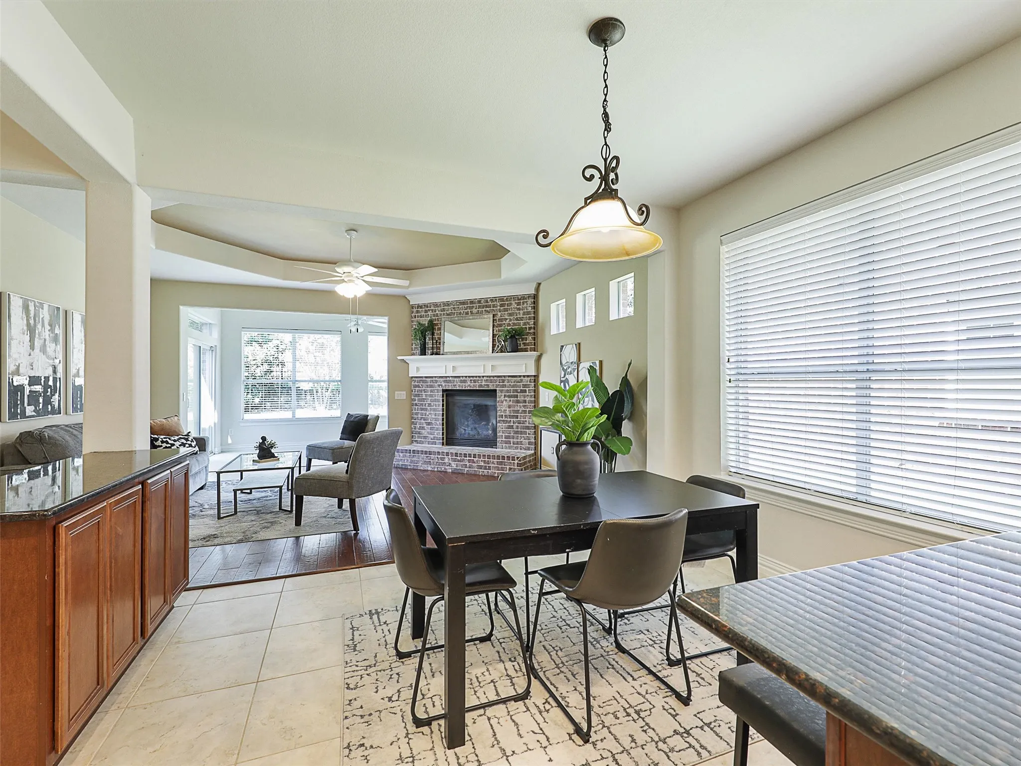 Dining space with a tray ceiling, a fireplace, a ceiling fan, and light tile patterned floors