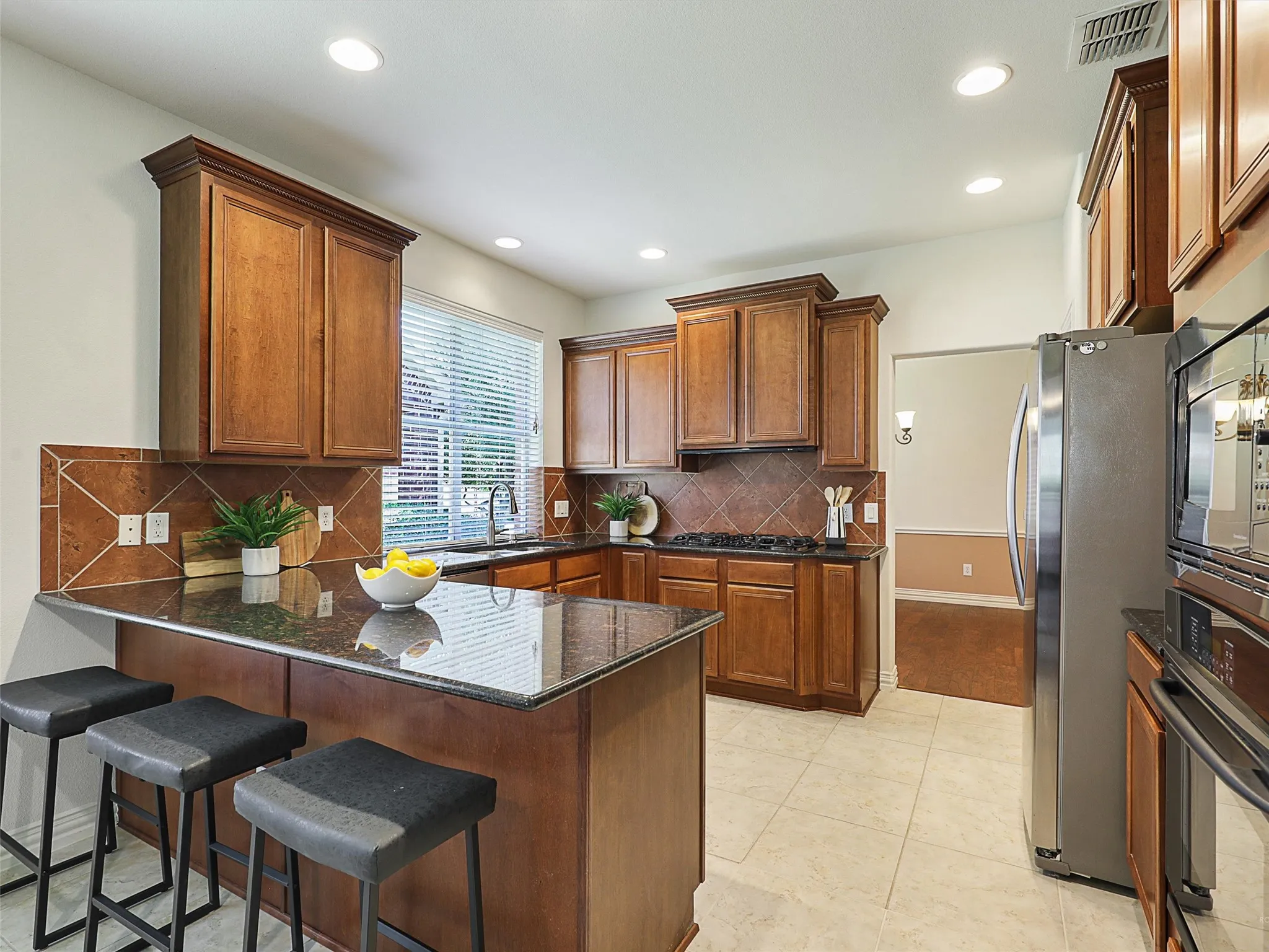 Kitchen with brown cabinets, dark stone countertops, a peninsula, black appliances, and backsplash