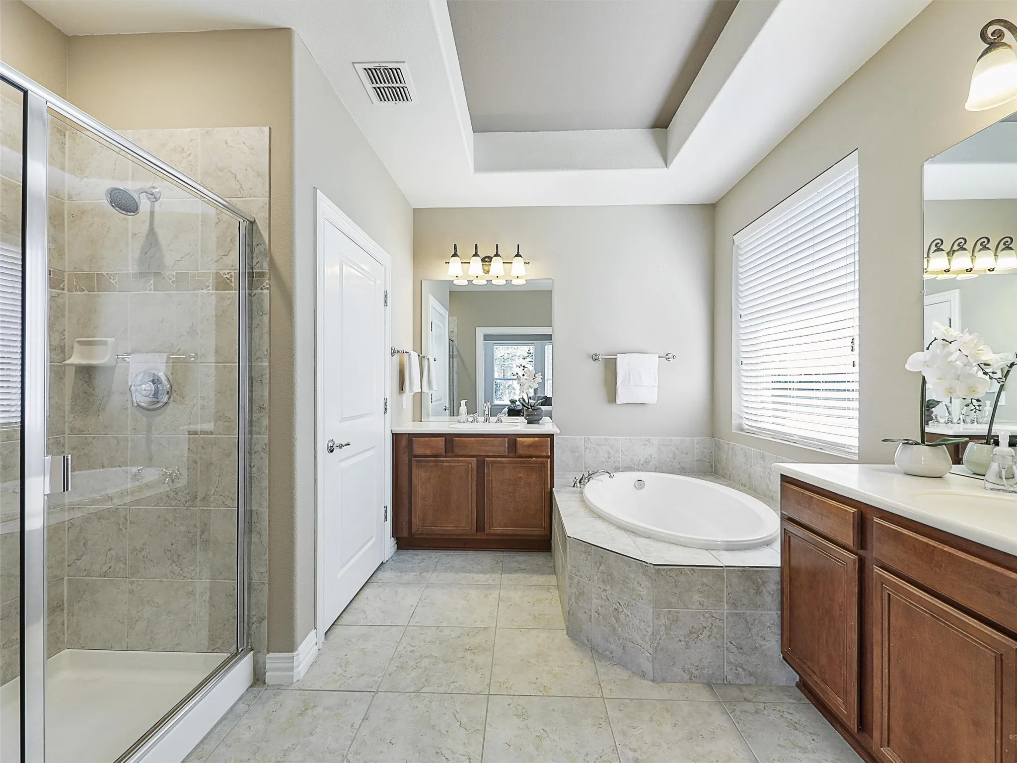Full bathroom with a garden tub, a shower stall, two vanities, light tile patterned floors, and a tray ceiling