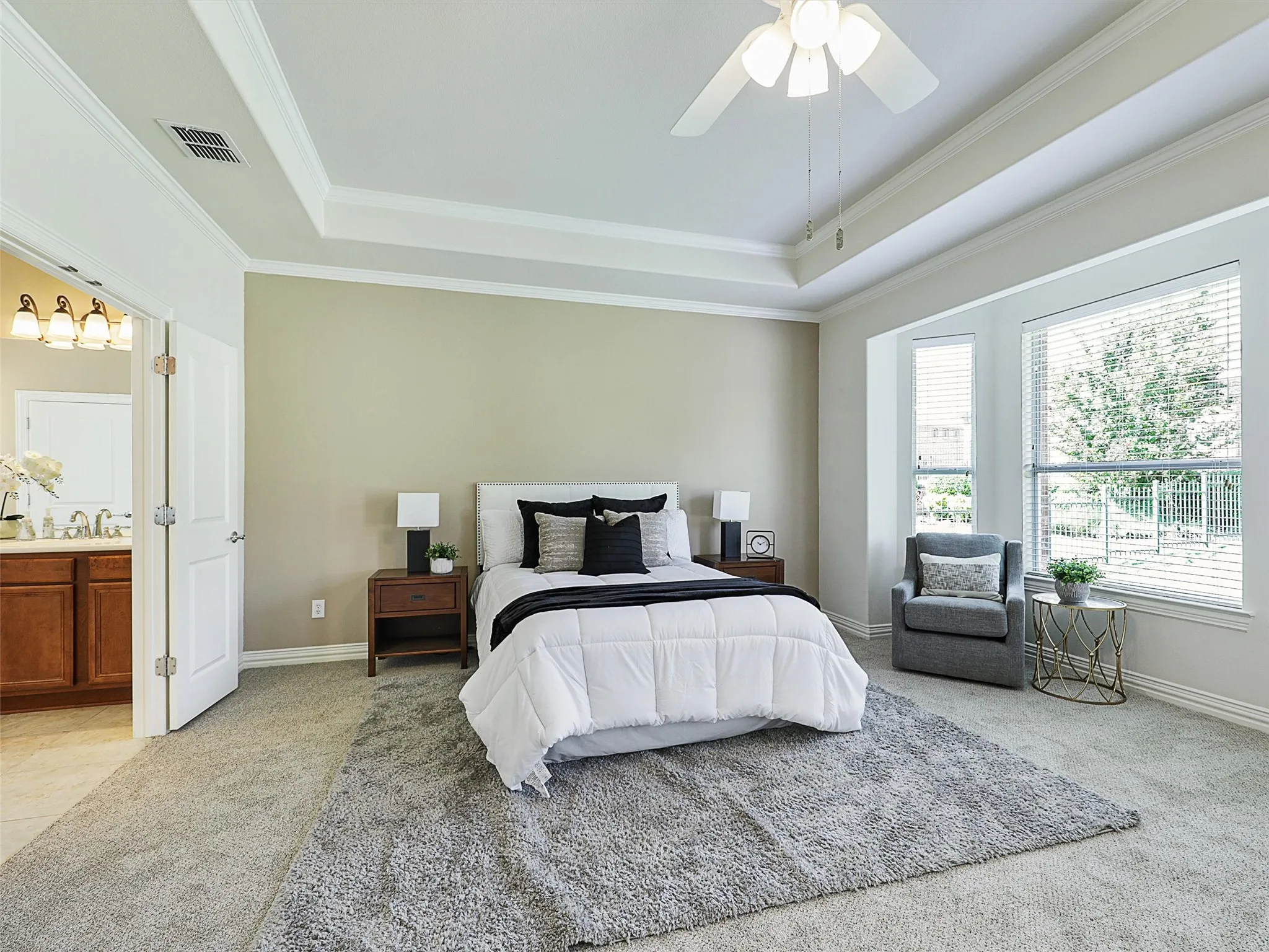 Bedroom with a raised ceiling, light carpet, a ceiling fan, crown molding, and ensuite bath