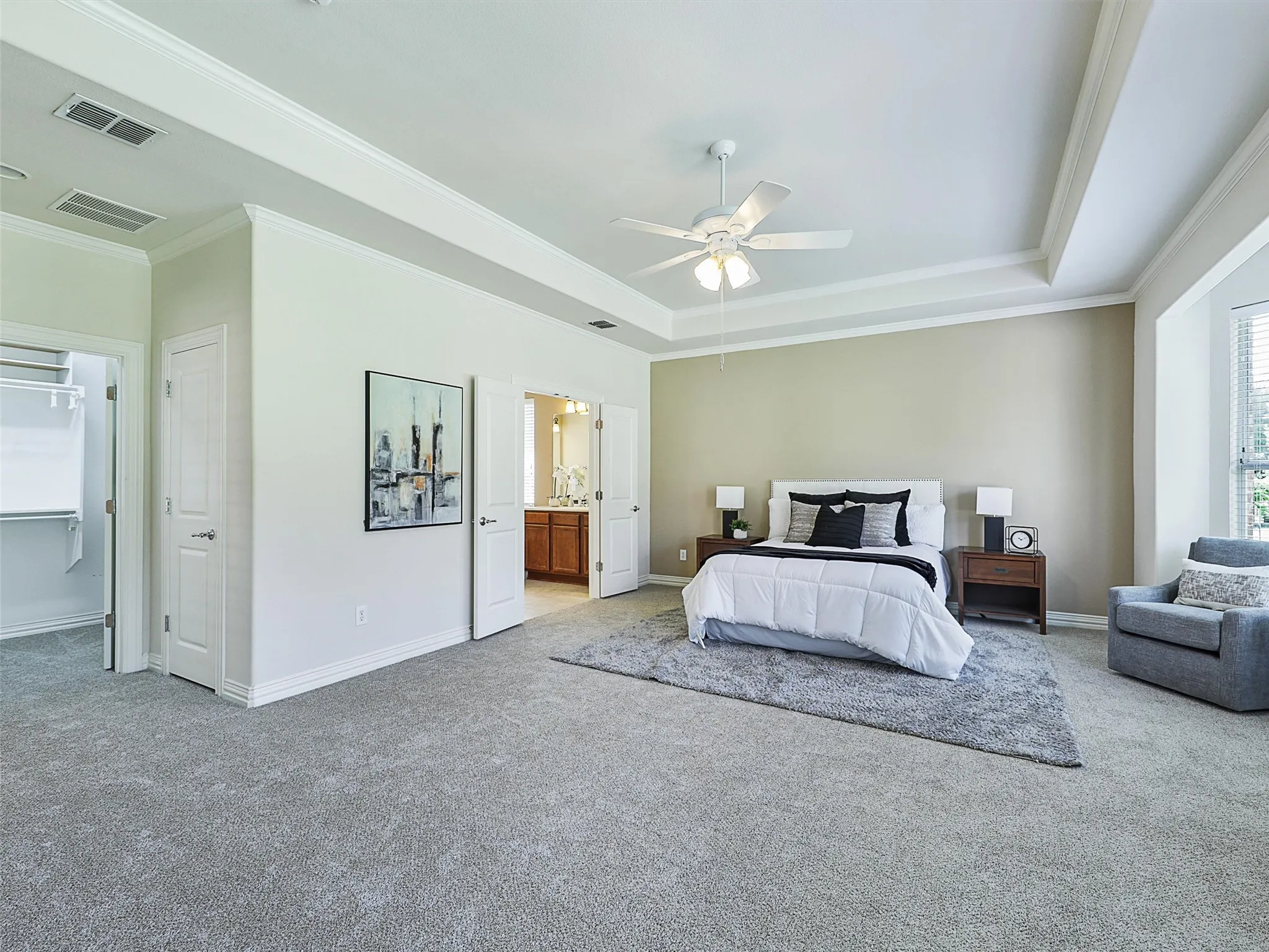 Primary Bedroom Carpeted bedroom with ornamental molding, a tray ceiling, ceiling fan, connected bathroom, and a walk in closet