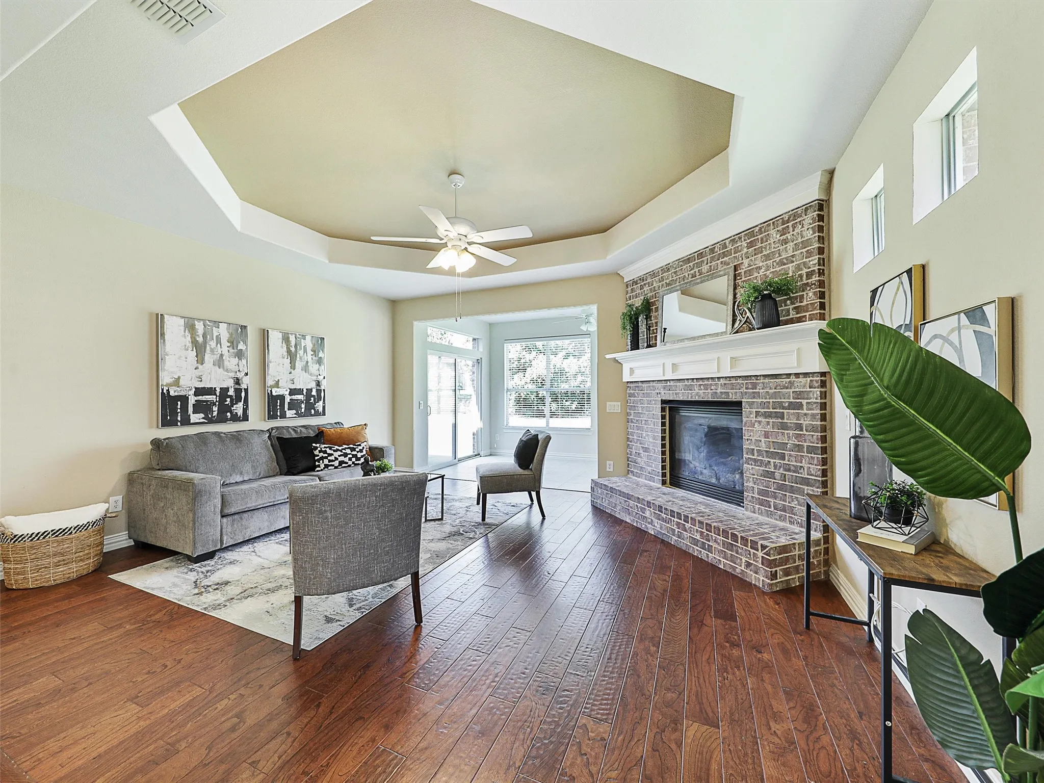 Living area featuring a raised ceiling, dark wood-type flooring, and a brick fireplace