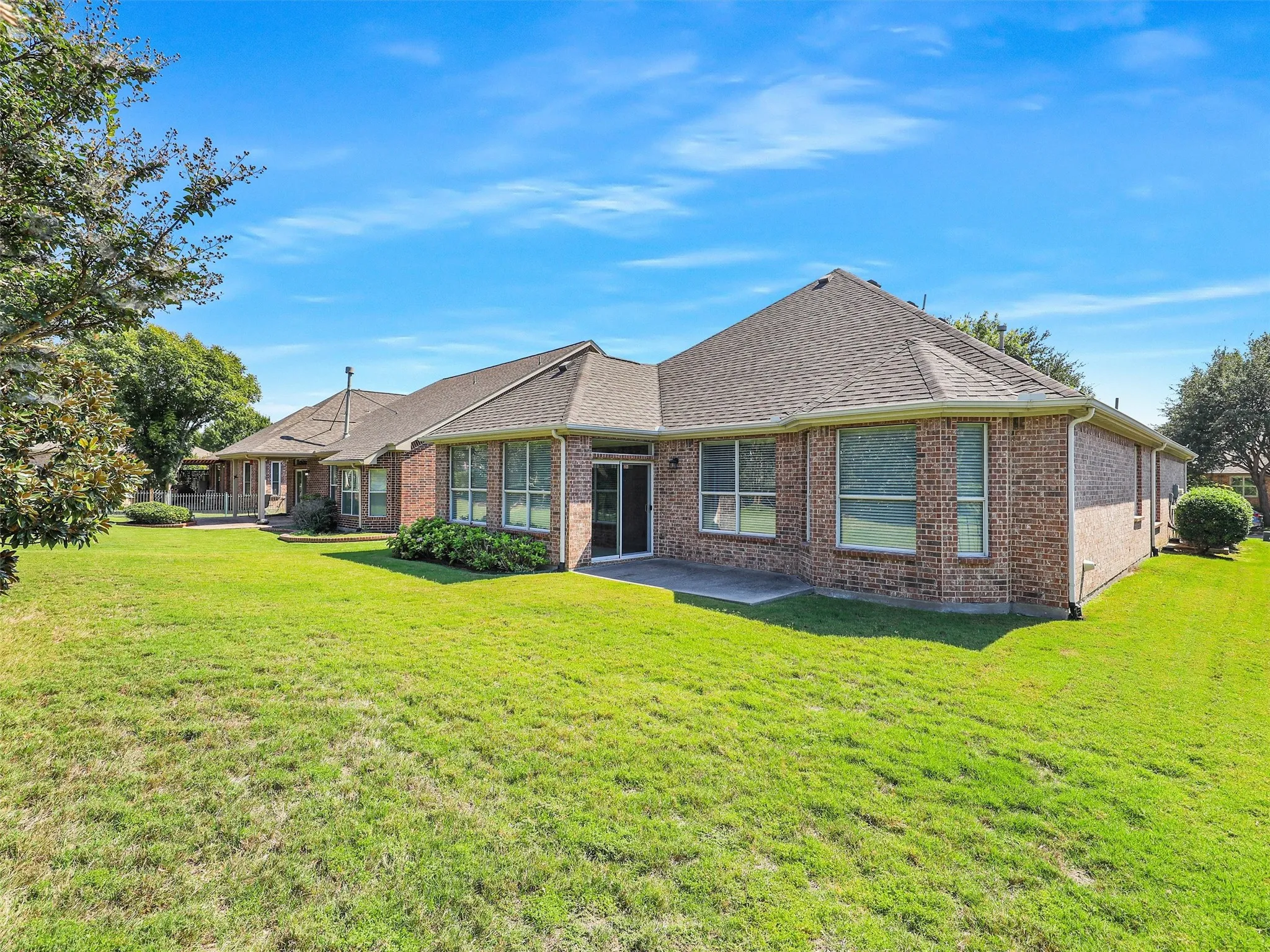 Rear view of property featuring a shingled roof, brick siding, a yard, and a patio